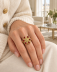 Bague Fergui fleur à six pierres rouges en plaqué or, portée à la main avec un cardigan écru dans un appartement parisien
