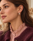 Créoles Marceau dorées portées avec une maille prune et une blouse rose à col victorien.