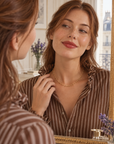Collier Miromesnil en plaqué or porté avec une chemise brune à rayures, reflet de la modèle dans un miroir d’appartement parisien