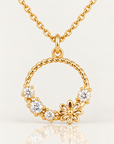 Gros plan du pendentif Solférino en plaqué or, cercle torsadé avec fleur aux pétales ajourés et quatre détails blancs, sur fond clair avec reflet miroir
