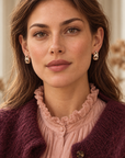 Boucles d’oreilles Marceau portées de face, avec une blouse rose à volants et un cardigan prune.