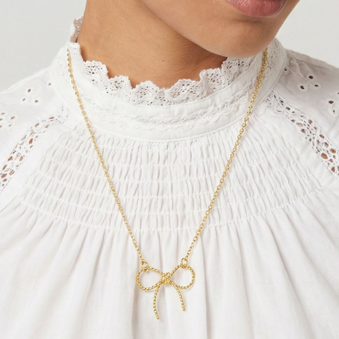 Collier Azurra avec pendentif nœud en plaqué or porté sur chemisier blanc – Jossepo