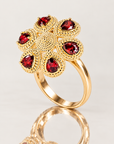 Bague Fergui en plaqué or 18 carats, fleur à six pierres rouges présentée debout sur une surface miroir