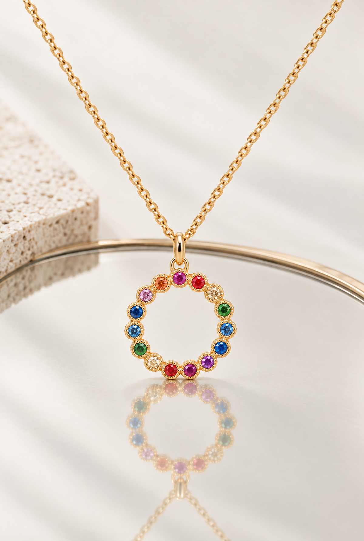 Collier Jasmin de 42 cm en plaqué or 18 carats, pendentif cercle à pierres multicolores présenté avec son reflet sur un miroir.