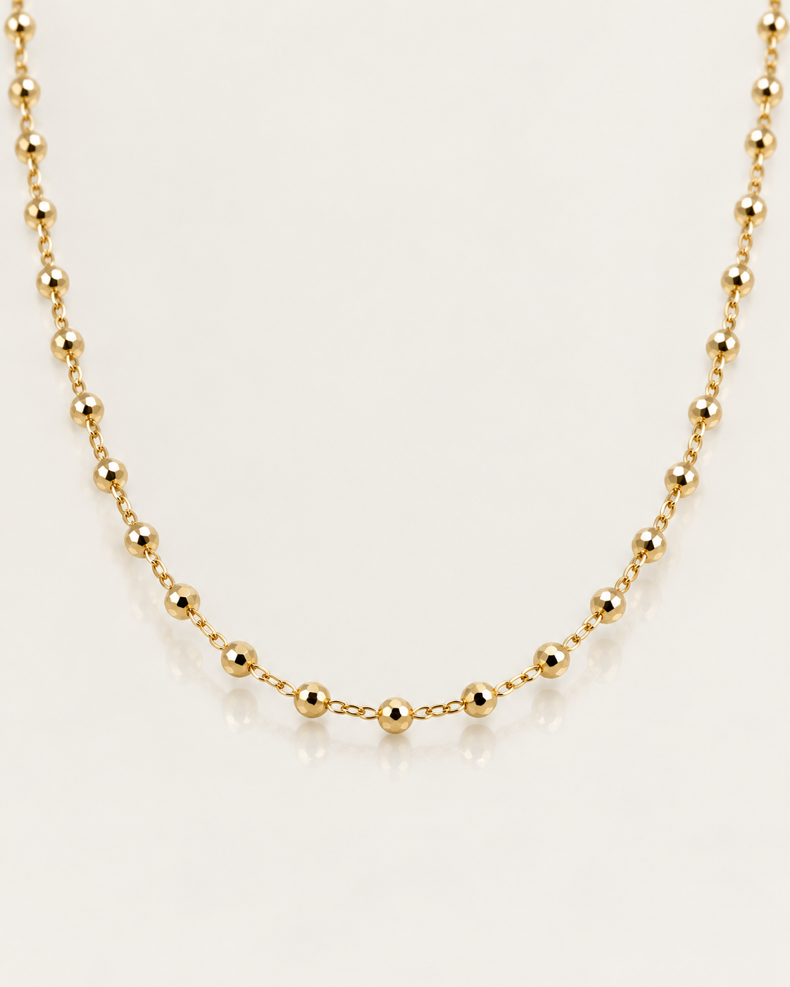 Détail du collier Miromesnil en plaqué or, petites boules dorées facettées et maillons fins sur une surface miroir