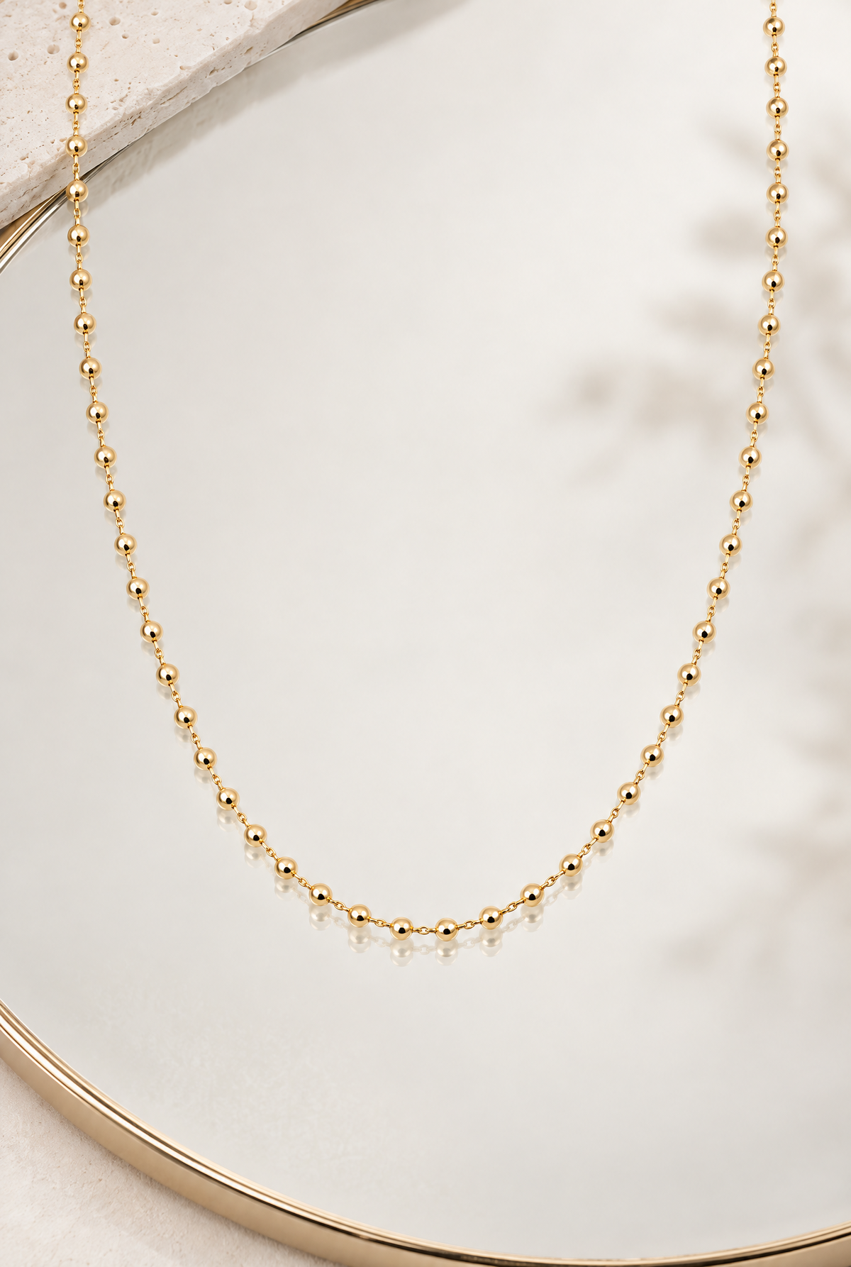 Collier Miromesnil en plaqué or à petites boules dorées, présenté sur un miroir avec reflet, vue d’ensemble