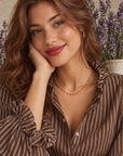 Collier Miromesnil à petites boules dorées porté avec une chemise brune à rayures et volants, portrait de la modèle