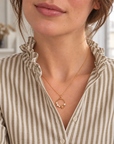 Collier Solférino au pendentif cercle floral porté avec une chemise à rayures kaki et beige et col volanté, vue rapprochée dans un appartement parisien