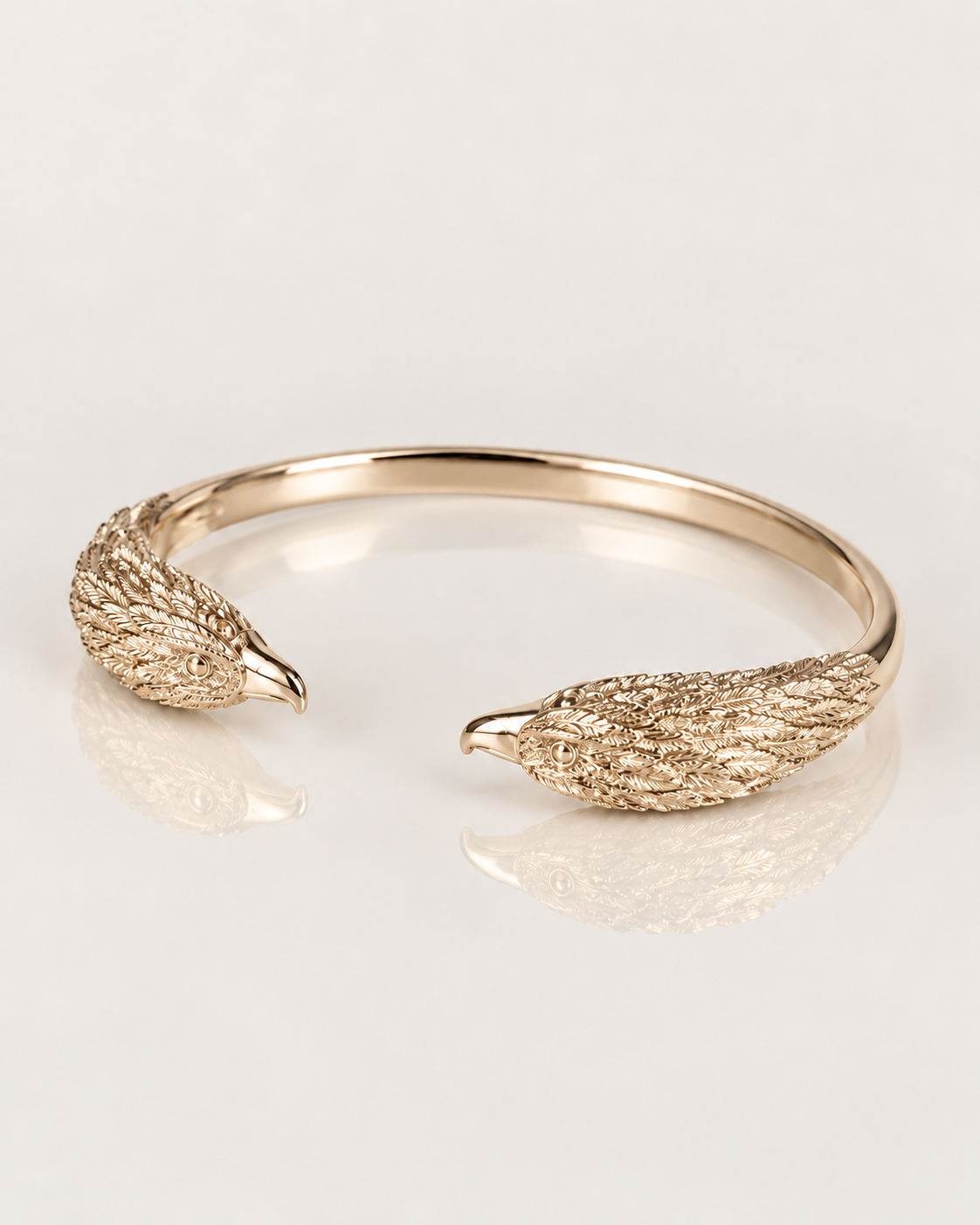 Jonc Aigle en plaqué or 18 carats, deux têtes d’aigle sculptées aux becs polis, vue de trois quarts avec reflet miroir