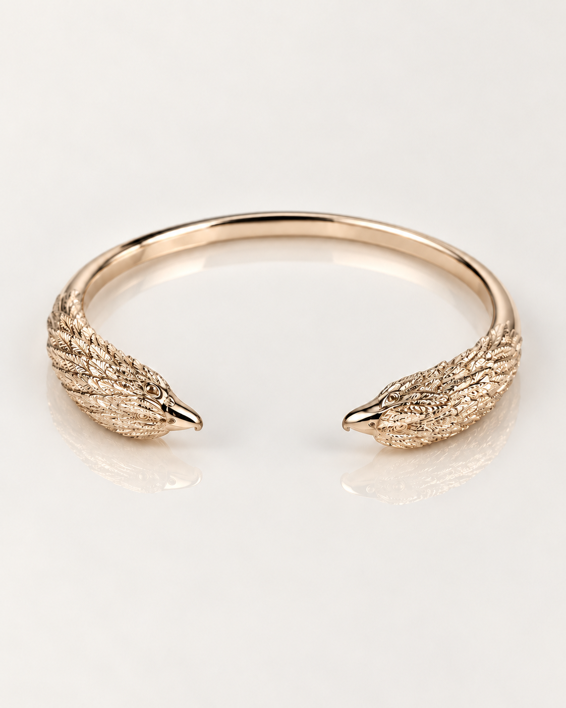 Jonc Aigle en plaqué or 18 carats, vue du dessus des deux têtes sculptées aux plumes en relief sur fond clair avec reflet miroir