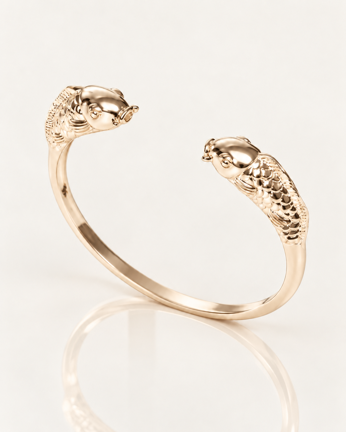 Jonc Poisson en plaqué or 18 carats, deux têtes de poisson sculptées et anneau lisse, vue de trois quarts sur fond clair avec reflet miroir